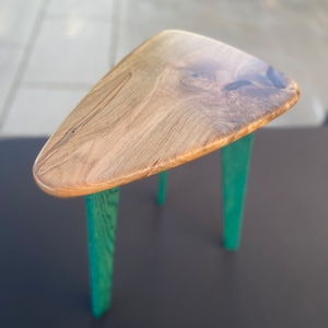 May include: A triangular wooden table with a natural wood finish and three teal green legs.