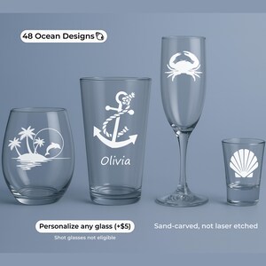 May include: Four clear drinking glasses with ocean-themed designs. The glasses include a stemless wine glass with a palm tree and dolphin design, a pint glass with an anchor, a champagne flute with a crab, and a shot glass with a seashell.