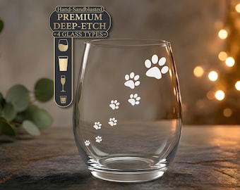 Puede incluir: Una copa de vino sin tallo transparente con un rastro de huellas de animales grabado en blanco. Sobre la copa, una etiqueta rectangular oscura muestra el texto Hand-Sandblasted PREMIUM DEEP-ETCH 4 GLASS TYPES con iconos de cuatro tipos de vidrio.