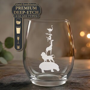 May include: A clear stemless wine glass featuring a white etched design of a vertical stack of animals including a hippopotamus, lion, giraffe, monkey, and bird. A dark rectangular label above reads Hand-Sandblasted PREMIUM DEEP-ETCH 4 GLASS TYPES.