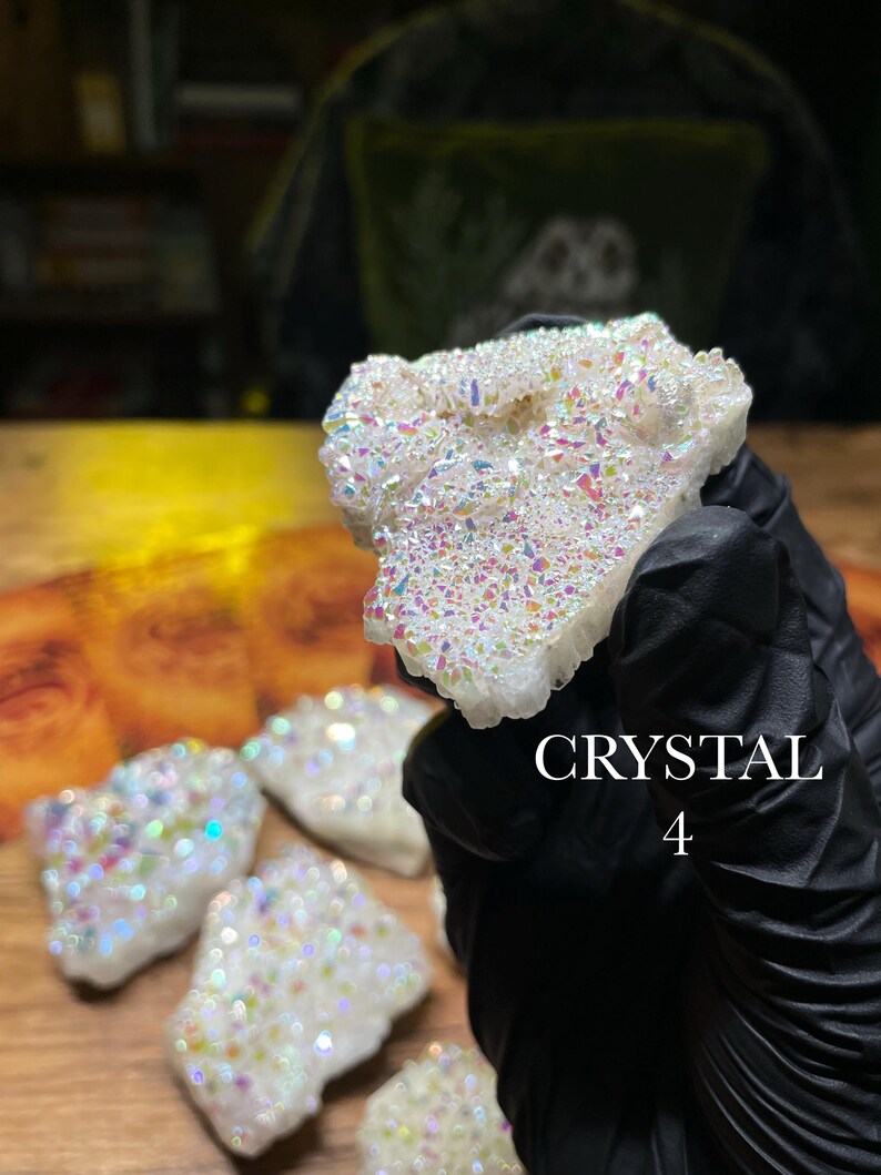 May include: A cluster of iridescent crystals with a white base and colorful, shimmering surfaces. The crystals are held by a gloved hand. The text "CRYSTAL 4" is visible in the image. Several other crystals are visible in the background.
