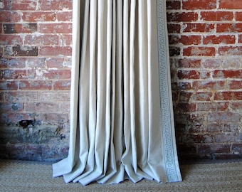May include: White linen curtains with a blue and white geometric pattern border. The curtains are hung on a black rod against a red brick wall.