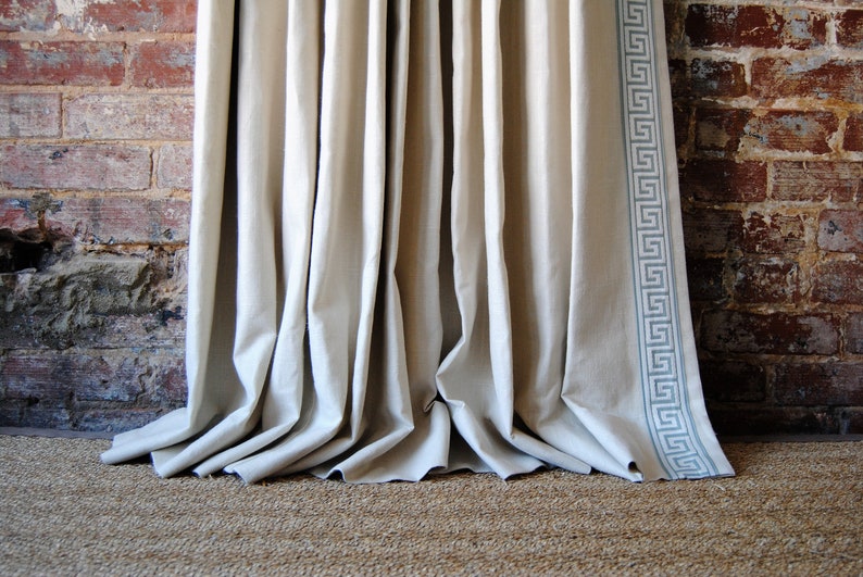 May include: A pair of white linen curtains with a gray Greek key trim hanging in front of a brick wall.