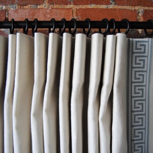 May include: White curtains with a geometric pattern border hanging on a black curtain rod.