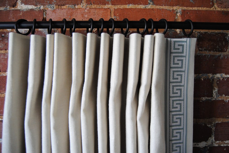May include: White curtains with a geometric pattern border hanging on a black curtain rod.