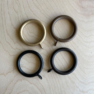 May include: Four curtain rings in different finishes: gold, brown, black, and dark brown. The rings are all the same size and have a simple, classic design.