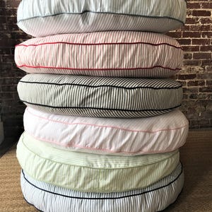 May include: A stack of six round pet beds with striped fabric covers. The beds are in various colors, including white, red, black, pink, green, and blue.