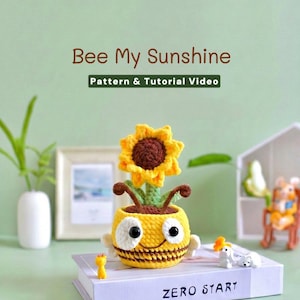 Op de afbeelding: Een gehaakte bijvormige plantenbak met een geel en bruin gestreept lichaam, grote zwarte ogen en een zonnebloem die uit de bovenkant groeit. De tekst "Bee My Sunshine" en "Pattern & Tutorial Video" is zichtbaar boven het object.