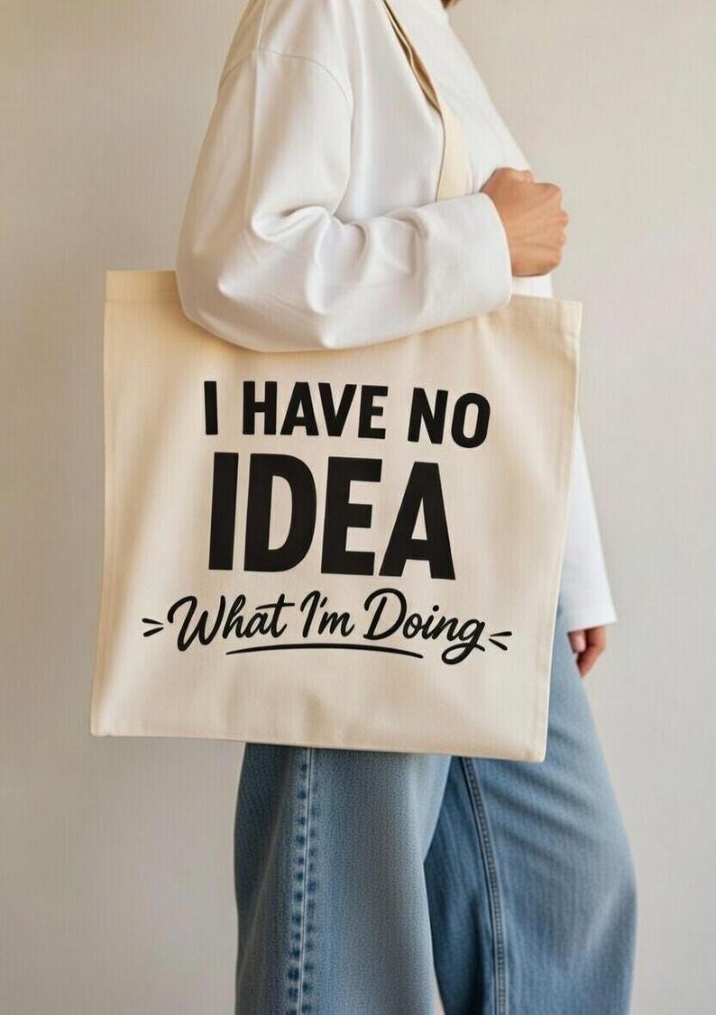 May include: Cream-colored tote bag with the text "I HAVE NO IDEA >What I'm Doing<". The bag has a rectangular shape and long straps. The text is in a bold, black font.