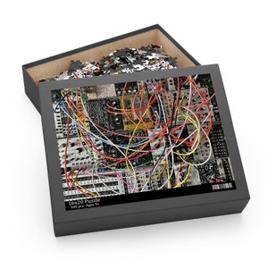 May include: A 500-piece jigsaw puzzle featuring a close-up of a colorful electronic music synthesizer with a tangle of wires. The puzzle box is black with white text that reads "16x20 Puzzle 500 pcs Ages 9+ ".