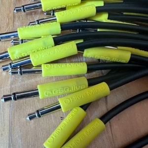 May include: A close-up of several black audio cables with yellow sleeves. The sleeves have the text "@bee.live Hive Mind" printed on them.