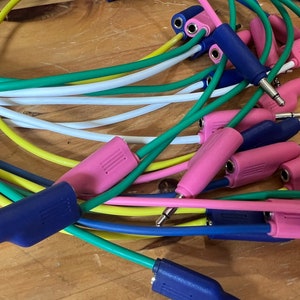 Puede incluir: Primer plano de un montón de cables de audio de colores con conectores de diferentes colores. Los cables son de color rosa, amarillo, verde, blanco y azul. Los conectores son todos de 3,5 mm.