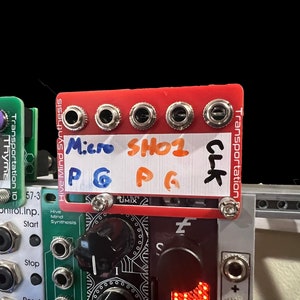 May include: A red, white, and black modular synthesizer module with four jacks labeled "Micro PG", "SHO1 PG", and "CLK". The module is labeled "Hive Mind Synthesis" and "Transportation".