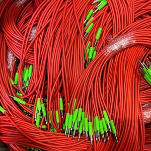 Może przedstawiać: Stos czerwonych kabli audio z zielonymi końcówkami. Kable są ze sobą połączone, z wieloma widocznymi. Zielone końcówki są równomiernie rozmieszczone i wydają się być wykonane z tworzywa sztucznego. Kable są prawdopodobnie do sprzętu audio.