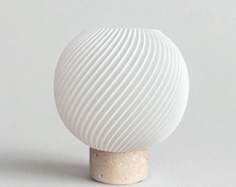 May include: A white, spherical vase with a textured, ridged surface. The vase sits atop a cylindrical, beige stone base. The design features a modern, minimalist aesthetic, suitable for home decor.