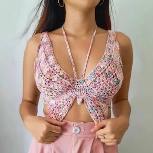 Puede incluir: Top de mariposa de ganchillo multicolor con cuello halter y cierre de lazo. El top se combina con pantalones de color rosa claro de cintura alta. El ganchillo presenta una mezcla de hilos rosas, azules y verdes.