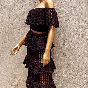 Peut inclure: Un ensemble deux pi&egrave;ces en crochet noir compos&eacute; d'un haut court &agrave; &eacute;paules d&eacute;nud&eacute;es avec des manches &agrave; volants et d'une jupe longue assortie &agrave; &eacute;tages. Le v&ecirc;tement pr&eacute;sente un motif en maille ouverte cr&eacute;ant un aspect textur&eacute; et superpos&eacute;.