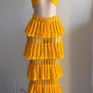 Peut inclure: Un ensemble deux pi&egrave;ces en crochet jaune vif compos&eacute; d'un haut bustier sans bretelles avec une petite fleur rose et d'une jupe longue assortie &agrave; quatre &eacute;tages avec un motif ajour&eacute; et une taille &agrave; cordon de serrage.