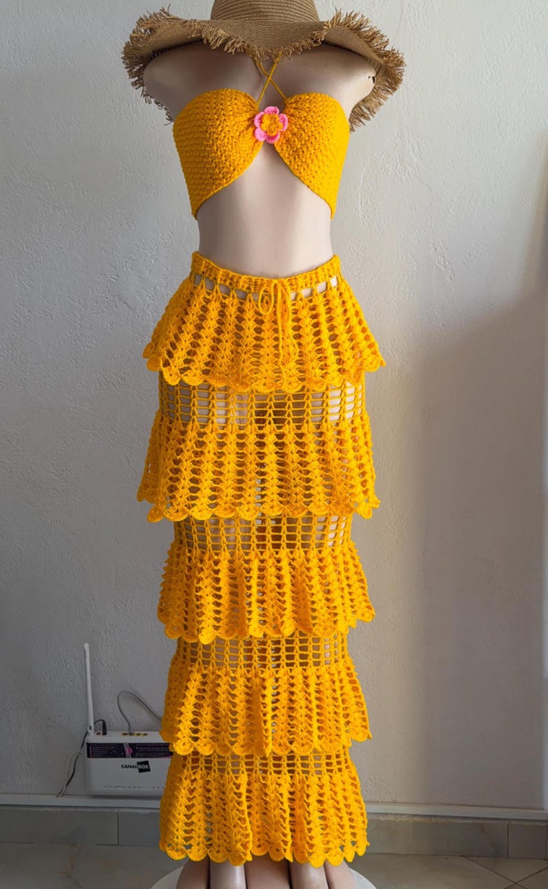 Peut inclure: Un ensemble deux pi&egrave;ces en crochet jaune vif compos&eacute; d'un haut bustier sans bretelles avec une petite fleur rose et d'une jupe longue assortie &agrave; quatre &eacute;tages avec un motif ajour&eacute; et une taille &agrave; cordon de serrage.