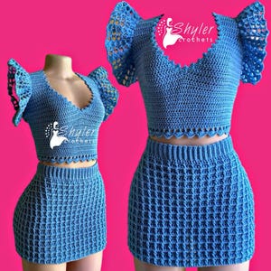 Puede incluir: Conjunto de dos piezas de crochet azul, compuesto por un top corto con borde festoneado y mangas con volantes, combinado con una minifalda a juego. El conjunto se muestra sobre un maniquí y sobre un fondo rosa. El top tiene cuello en V y el nombre de la marca "Shyler crochets".