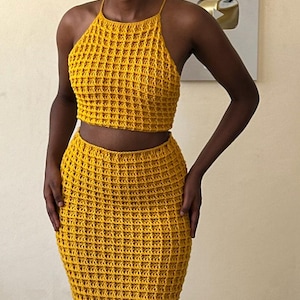 May include: Mustard yellow crochet halter top and matching skirt. The two-piece set features a textured, open weave design. The top is a cropped style, and the skirt is a fitted, floor-length design. The outfit is made of a soft, breathable material.