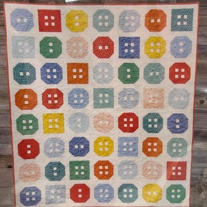May include: A colorful quilt with a button design. The quilt features various colored squares and octagons with button details. The text "Button Up" is at the top, and "A fat quarter quilt in 3 sizes" is at the bottom.