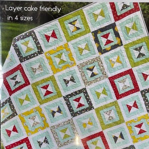 May include: A colorful quilt with a repeating square pattern. Each square features a bow tie design in red, green, yellow, and black, set against a light blue background. The word "Dixie" is at the top, with "Layer cake friendly in 4 sizes" below.