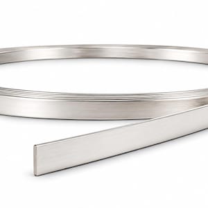 May include: A continuous, coiled strip of brushed silver-toned metal with a flat, rectangular profile. The material has a smooth, matte finish and is wound into a circular shape, with one end extending outward from the main coil structure.