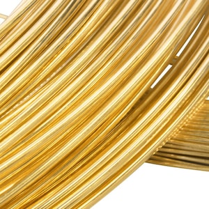 May include: A coil of shiny, metallic gold-colored wire arranged in multiple circular loops. The wire has a smooth, reflective surface and a consistent cylindrical shape, creating a dense, layered pattern of parallel golden lines throughout.