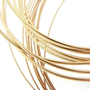 May include: A coil of thin, flexible gold-colored wire arranged in overlapping circular loops. The metallic strands have a smooth, reflective surface and a consistent gauge, creating a series of curved lines that intersect and layer over one another.