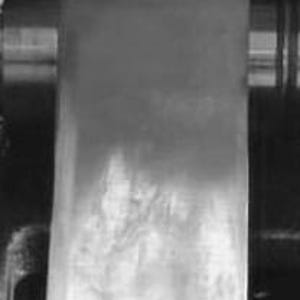 Puede incluir: Primer plano de un rodillo met&aacute;lico utilizado en una prensa de impresi&oacute;n. El rodillo est&aacute; cubierto con una fina capa de tinta, que se est&aacute; transfiriendo a una hoja de papel.