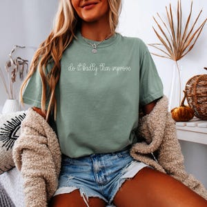 May include: Sage green t-shirt with the text "do it badly then improve" in a handwritten style. The shirt is paired with denim shorts and a beige cardigan. The overall aesthetic is casual and comfortable.