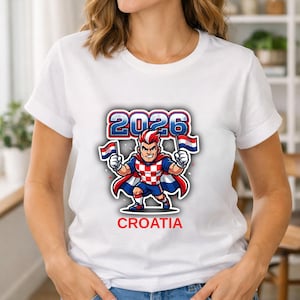 May include: White t-shirt featuring a cartoon superhero with the text "2026 CROATIA". The superhero is wearing a red and white checkered outfit and holding two Croatian flags. The design is in red, white and blue.