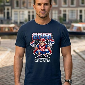 Puede incluir: Camiseta azul marino con un personaje de dibujos animados con los colores de Croacia, sosteniendo banderas y el texto "2026" encima de "CROATIA". El dise&ntilde;o est&aacute; centrado en la camiseta.