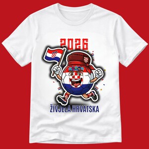 May include: White t-shirt with a cartoon soccer ball character in the Croatian flag design, holding a flag and running. The text "2026" is above the character, and "ŽIVJELA HRVATSKA" is below.