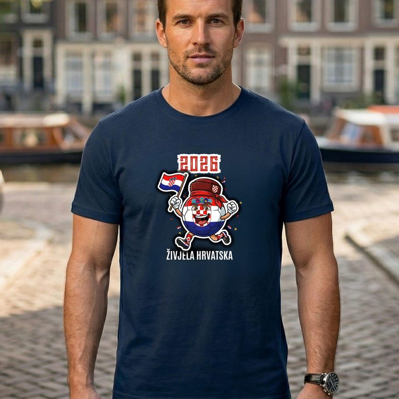 May include: Navy blue t-shirt with a cartoon soccer ball character wearing a hat and holding a Croatian flag. The shirt has the text "2026" and "ŽIVJELA HRVATSKA". The shirt is being worn by a person.