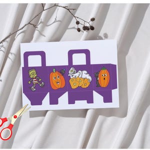 Puede incluir: Una caja de regalo blanca y morada con temática de Halloween con ilustraciones de dibujos animados de un zombi, calabazas, fantasmas y un gato negro. Unas tijeras con mango rojo están en primer plano. La caja tiene una asa y está diseñada para plegarse.