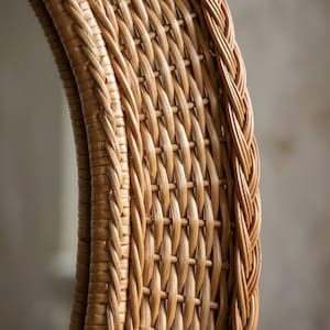 May include: A round mirror featuring a light brown woven wicker frame. The frame displays a detailed lattice pattern with a thick, braided border along the outer and inner edges, showcasing the natural texture and tan colour of the material.