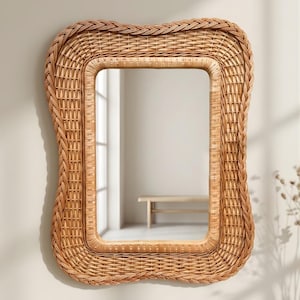 May include: A rectangular wall mirror featuring a light brown woven rattan frame with a wavy, organic edge. The frame consists of multiple layers of intricate wicker detailing, surrounding a clear, reflective glass centre surface.