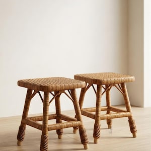 May include: Two square stools crafted from light brown woven rattan. Each stool features a flat, tightly woven seat and four legs reinforced with horizontal crossbars. The lower portion of each leg is wrapped in a decorative, thicker rattan coil.