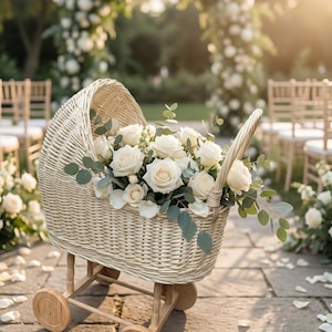 Könnte beinhalten: Ein geflochtener Babywagen, gefüllt mit weißen Rosen und Grünzeug. Der Wagen hat Holzräder. Die Szene spielt sich im Freien ab, mit einem Blumenbogen und Stühlen im Hintergrund, was auf eine Hochzeit oder Veranstaltung hindeutet.
