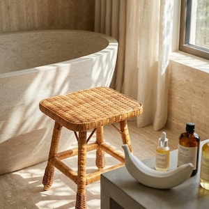 May include: A square-topped stool constructed from woven light brown rattan with four sturdy legs connected by horizontal support bars. The stool features a natural textured finish and a simple, functional design suitable for various interior spaces.