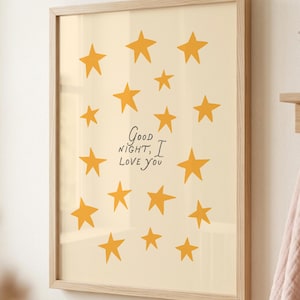 May include: A rectangular wall art print in a light wood frame featuring a cream-colored background with scattered mustard yellow stars and the black handwritten text Good Night, I Love You centered in the middle of the composition.