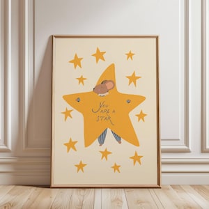 Puede incluir: Impresión artística enmarcada con una ilustración caprichosa. Un personaje de ratón viste un disfraz de estrella con el texto "You are a Star". La obra de arte tiene un fondo crema con estrellas amarillas.