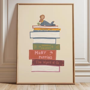 Könnte beinhalten: Ein gerahmter Kunstdruck auf cremefarbenem Hintergrund zeigt einen Bücherstapel, auf dem eine braune Maus in blau gestreiftem Schlafanzug liest. Die Buchrücken tragen die Titel Charlotte's Web, The Very Hungry Caterpillar, Curious George, Mary Poppins und The Wizard of Oz.