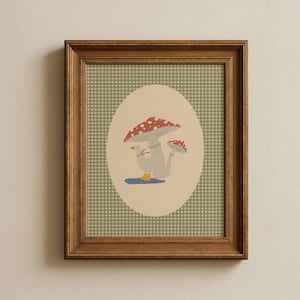 May include: A framed print featuring a whimsical illustration of a goose standing under two red and white spotted mushrooms. The goose is wearing a red bow. The background is a green and white checkered pattern.