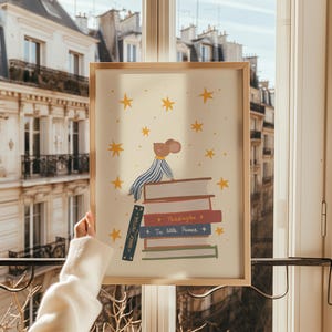 May include: A framed art print featuring a cartoon mouse wearing a striped shirt, sitting atop a stack of books. The books include titles like "Harry Potter," "Paddington," and "The Little Prince." The background is a light beige with yellow stars.