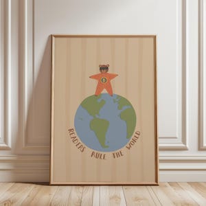 May include: A framed art print featuring a cartoon bear superhero standing on a globe. The bear wears a star-shaped outfit and sunglasses. The globe is blue and green, with the words "Readers Rule the World" in a circular pattern.