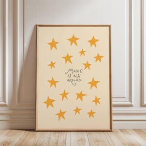 Könnte beinhalten: Ein gerahmter Druck mit cremefarbenem Hintergrund und gelben Sternen. Der Schriftzug "MAGIC IS ALL AROUND" ist in Schwarz gehalten. Der Rahmen ist braun, und der Druck lehnt an einer weißen Wand mit Zierleisten.
