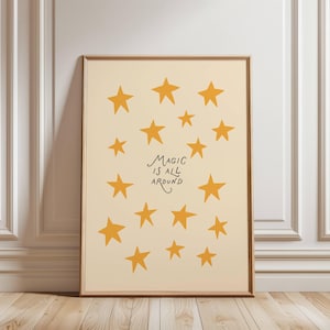 May include: A framed print featuring a cream-colored background with numerous yellow stars of varying sizes. The phrase "MAGIC IS ALL AROUND" is written in black script. The frame is a warm brown color, and the print is leaning against a white wall.